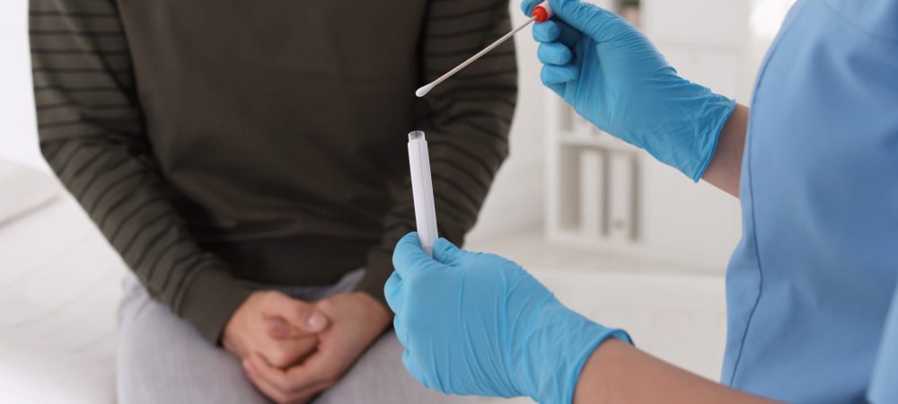 Doctor taking sample for STD testing from man in clinic, closeup