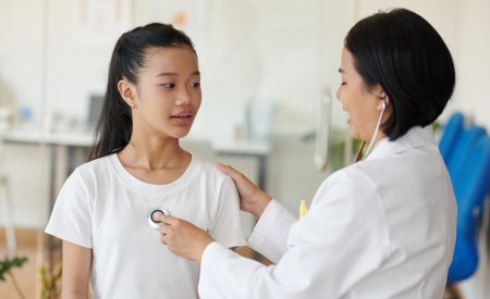 Positive pediatrician listening to heartbeat of Vietnamese teenage girl