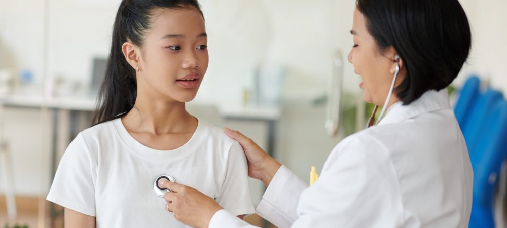 Positive pediatrician listening to heartbeat of Vietnamese teenage girl
